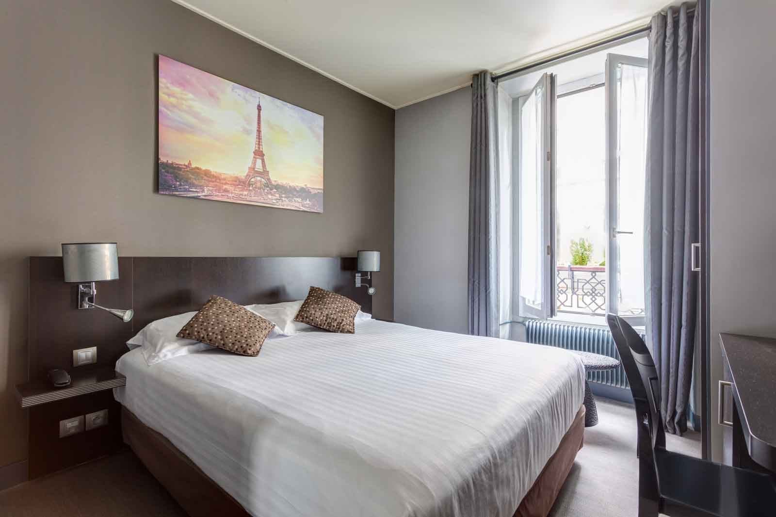 Chambre d'hôtel aux murs taupe avec un grand lit double, un tableau de la tour Eiffel et une fenêtre ouverte sur un balcon parisien.