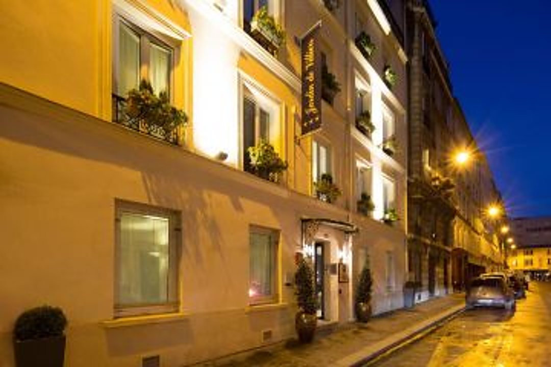 Façade jaune d'un petit hôtel avec jardinières fleuries et enseigne verticale, photographiée au crépuscule dans une rue éclairée.