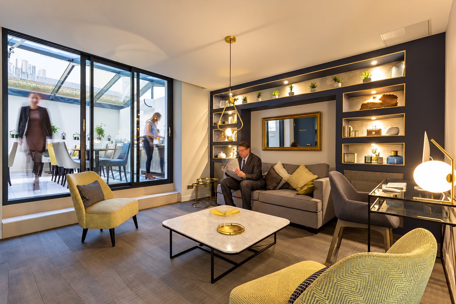 Un salon moderne aux tons jaunes et bleu nuit, avec un homme lisant le journal sur un canapé et une terrasse vitrée en arrière-plan.