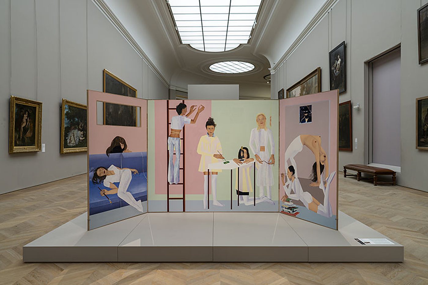 Un grand triptyque peint représentant des femmes en blanc dans des scènes colorées, présenté sur une estrade au centre d'une galerie de musée aux murs ornés de tableaux anciens.